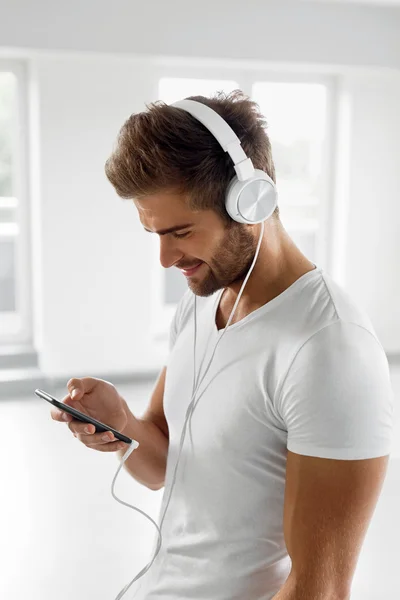 Homem ouvindo música em fones de ouvido usando telefone celular dentro de casa — Fotografia de Stock