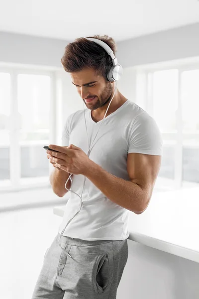 Música Ouvindo. Homem em fones de ouvido usando telefone celular dentro de casa — Fotografia de Stock