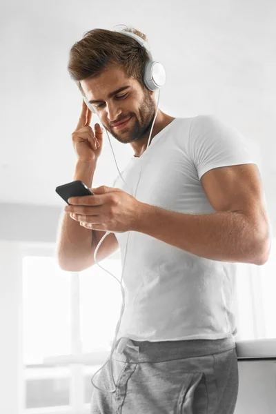 Poslech hudby. Muž ve sluchátkách s mobilním telefonem v interiérech — Stock fotografie