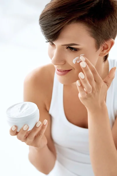 Cura della pelle di bellezza. Bella donna che applica crema cosmetica per il viso — Foto Stock