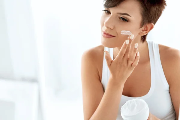 Cura della pelle di bellezza. Bella donna che applica crema cosmetica per il viso — Foto Stock