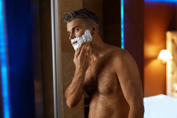 Muž používající holicí krém na obličej v koupelně. Péče o kůži mužů — Stock fotografie