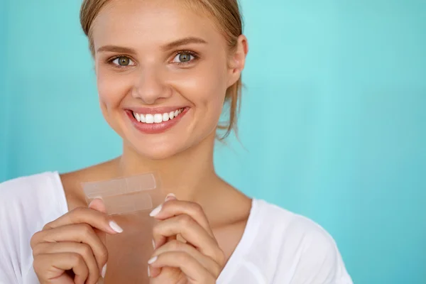 Blanqueamiento de dientes. Hermosa mujer sonriente sosteniendo tira blanqueadora —  Fotos de Stock