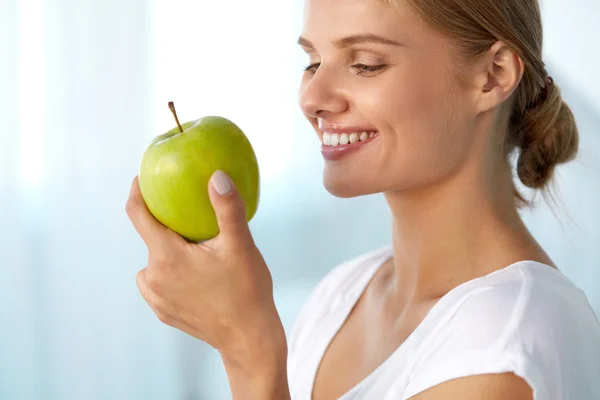 녹색 사과를 먹는 흰색 치아를 가진 아름다운 미소 짓는 여자 — 스톡 사진
