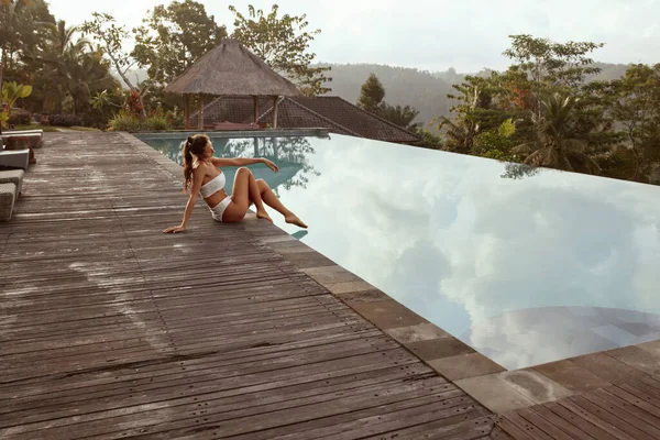 Beautiful Girl In Bikini Sitting Near Infinity Pool In Bali, Indonésia. jovem mulher com sexy corpo no branco maiô relaxante no tropical resort retrato. — Fotografia de Stock