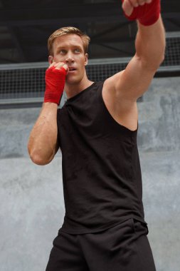 Genç adam boks pozisyonunda durur ve yumruk egzersizi yapar. Yakışıklı beyaz tenli kaslı sporcu. Moda sporunda güçlü vücut ve beton duvara karşı bileklerine sarılı..