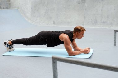 Beton Duvara Karşı Yoga Mattı Egzersizi Yapan Genç Adam. Yakışıklı beyaz tenli güçlü kaslı sporcu. Moda sporu kıyafetleri, yoğun antrenmandan önce ısınıyor..