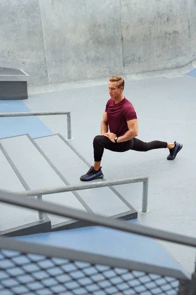 Jovem se alongando perto de degraus de concreto ao ar livre. Bonito desportista caucasiano com corpo muscular forte na moda Sportswear aquecendo antes do treino intenso. — Fotografia de Stock