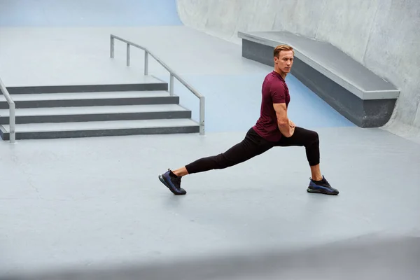 Молодий чоловік розтягується біля бетонних сходів на відкритому повітрі. Красивий Кавказький спортсмен з сильним м'язовим тілом в моді Спортивний одяг Утеплення до інтенсивного тренування . — стокове фото
