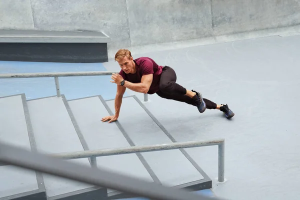 Jeune homme faisant la planche près de marches en béton à l'extérieur. beau sportif caucasien avec fort corps musculaire dans la mode vêtements de sport échauffement avant entraînement intense. — Photo