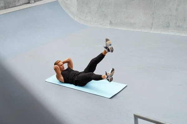 Jeune homme faisant Abs séance d'entraînement sur tapis de yoga contre le mur de béton à l'extérieur. bel homme de sport caucasien avec un corps musculaire fort dans la mode vêtements de sport échauffement avant l'entraînement fonctionnel intense. — Photo