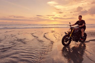 Ocean Beach 'teki Adam ve Motosiklet Güzel Tropikal Gün Batımında. Endonezya, Bali 'de Kum Sahili' nde Motosikletli Yakışıklı Motorcu.