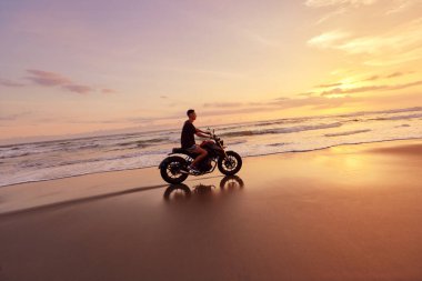Ocean Beach 'teki Adam ve Motosiklet Güzel Tropikal Gün Batımında. Endonezya, Bali 'de Kum Sahili' nde Motosikletli Yakışıklı Motorcu.