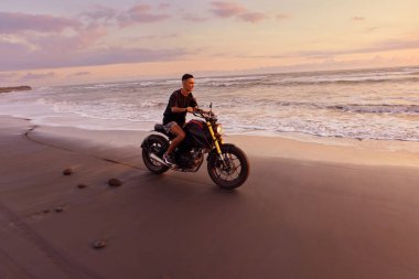 Ocean Beach 'teki Adam ve Motosiklet Güzel Tropikal Gün Batımında. Endonezya, Bali 'de Kum Sahili' nde Motosikletli Yakışıklı Motorcu.