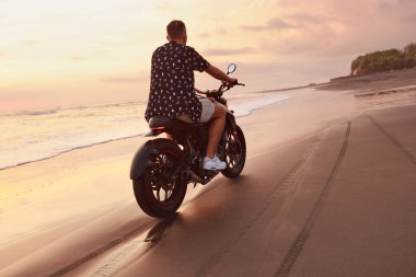 Ocean Beach 'teki Adam ve Motosiklet Güzel Tropikal Gün Batımında. Endonezya, Bali 'de Kum Sahili' nde Motosikletli Yakışıklı Motorcu.