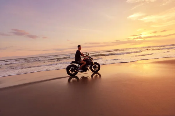 Homme et moto sur Ocean Beach au beau coucher de soleil tropical. Beau motard sur la moto sur la côte de sable à Bali, Indonésie. — Photo