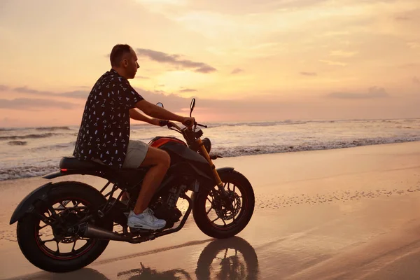 Ocean Beach 'teki Adam ve Motosiklet Güzel Tropikal Gün Batımında. Endonezya, Bali 'de Kum Sahili' nde Motosikletli Yakışıklı Motorcu.