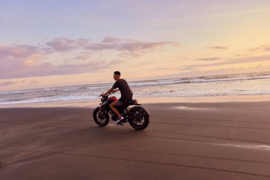 Ocean Beach 'teki Adam ve Motosiklet Güzel Tropikal Gün Batımında. Motosikletli Siluet Kum kıyısında Deniz kenarında Endonezya Bali 'de.