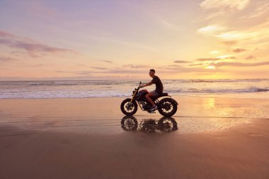 Ocean Beach 'teki Adam ve Motosiklet Güzel Tropikal Gün Batımında. Motosikletli Siluet Kum kıyısında Deniz kenarında Endonezya Bali 'de.