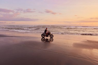 Ocean Beach 'teki Adam ve Motosiklet Güzel Tropikal Gün Batımında. Motosikletli Siluet Kum kıyısında Deniz kenarında Endonezya Bali 'de.