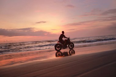 Ocean Beach 'teki Adam ve Motosiklet Güzel Tropikal Gün Batımında. Motosikletli Siluet Kum kıyısında Deniz kenarında Endonezya Bali 'de.