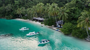 Kaimana Adası 'ndaki palmiye ağaçları arasında kulübeleri olan, Okyanus kıyısında tekneleri olan göl, Raja Ampat. Endonezya 'nın Papua kentindeki Tropikal tatil beldesi yakınlarındaki Turkuaz Denizi' ndeki Drone on Water Transport 'tan çarpıcı bir görüntü.