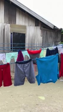 Kaimana Adası 'ndaki ahşap eve karşı çamaşır ipinde renkli kıyafetler. Papua, Endonezya 'daki Kırsal Bahçenin Dikey Videosu.