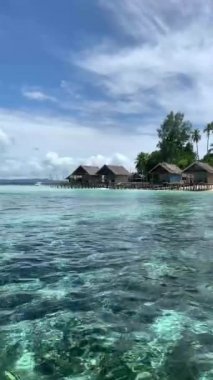 Kaimana Adası 'ndaki Ocean Beach' te kulübeleri olan bir göl. Papua, Endonezya 'da Turkuaz Denizi ve Bungalovlu Resimli Tropikal Tatil Köyü.