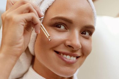Yüzüne pipetten serum kolajen nemlendiricisi düşüren bir kız. Kafasına havlu sarılmış genç ve güzel bir kadın. Yüz bakımı kavramı