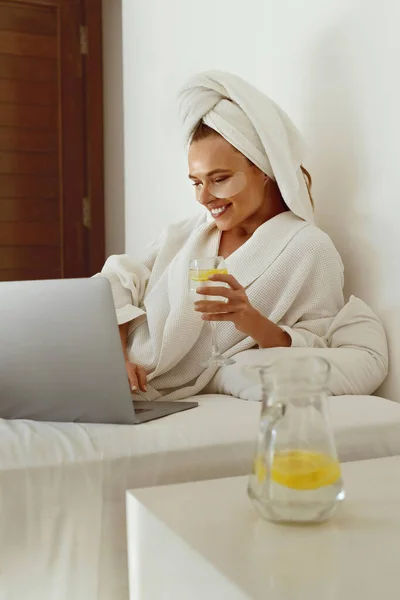Uśmiechnięta Europejka Szlafroku Używa Laptopa Pije Lemoniadę Leżąc Łóżku Młoda — Zdjęcie stockowe