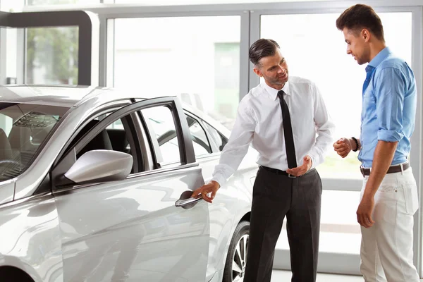 Продавец автомобилей показывает молодому человеку новый автомобиль — стоковое фото