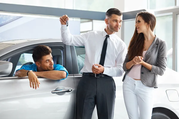 Sprzedawca samochodów zaprasza klientów w salonie. — Zdjęcie stockowe