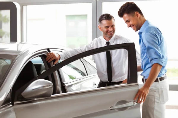 Concesionario de vehículos Mostrando al hombre joven un coche nuevo — Foto de Stock