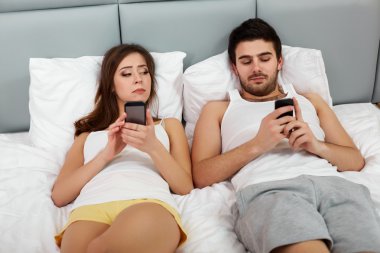 Cep telefonlarıyla bir yatakta mutlu çift