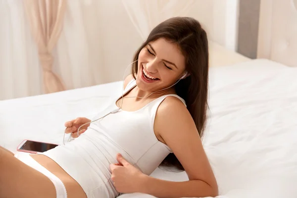 Mooie vrouw luistert een muziek liggend op het bed — Stockfoto