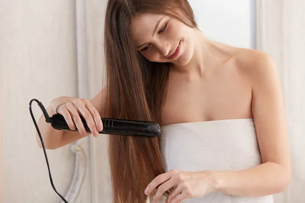 Woman straightening hair with straightener — Stock Photo, Image