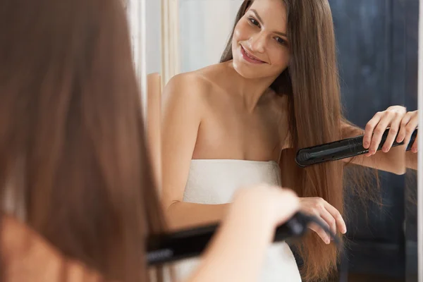 Woman straightening hair with straightener — Stock Photo, Image