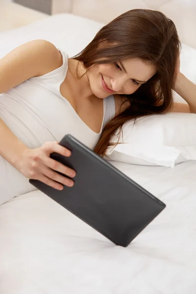 Mujer joven sonriente con la tableta en su cama — Foto de Stock