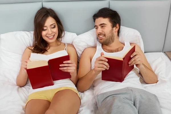 Pareja feliz sentada en la cama leyendo libros en casa —  Fotos de Stock