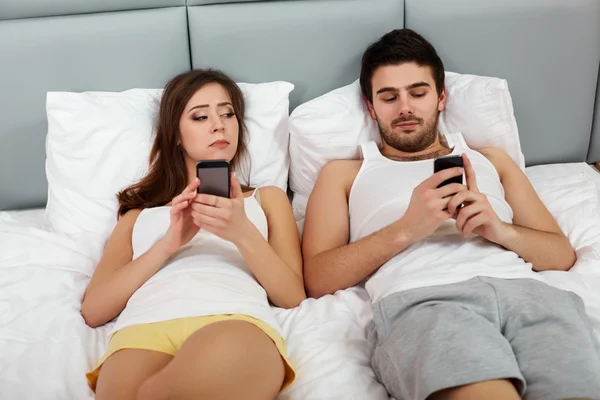 Casal feliz em uma cama com telefones celulares — Fotografia de Stock