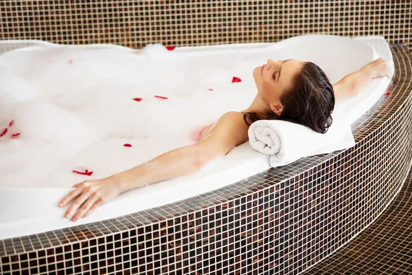 Mulher relaxante em banho de espuma com pétalas de rosa. Cuidado com o corpo — Fotografia de Stock