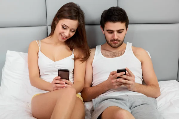 Casal feliz em uma cama com telefones celulares — Fotografia de Stock