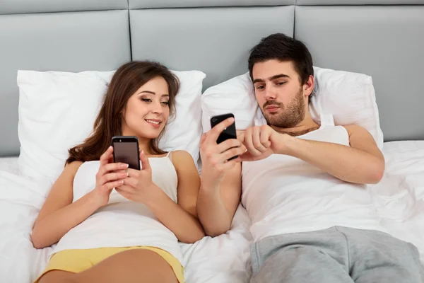 Casal feliz em uma cama com telefones celulares — Fotografia de Stock