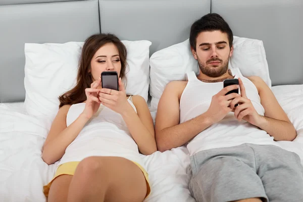 Casal feliz em uma cama com telefones celulares — Fotografia de Stock