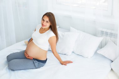 Pregnant Happy smiling Woman sitting on a bed and caressing her