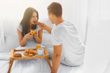 Young man feeding woman in bed