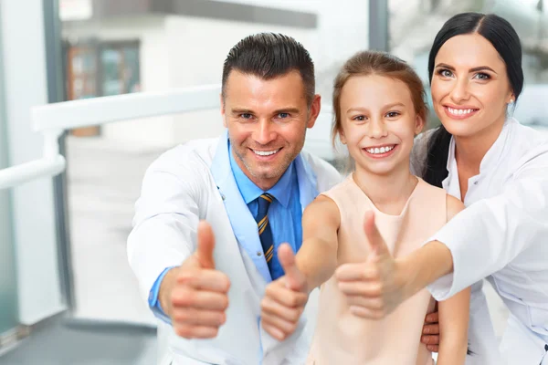 Médico dentista, assistente e menina todos sorrindo para a câmera — Fotografia de Stock