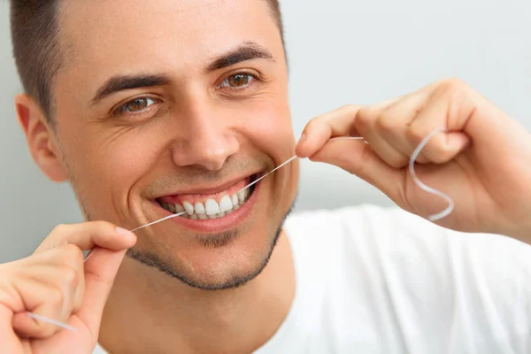 Fechamento do jovem a usar fio dental nos dentes. Limpar os dentes com den — Fotografia de Stock