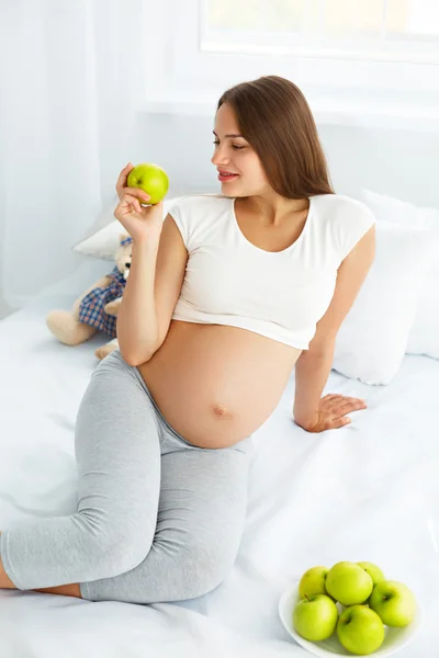 Jeune femme enceinte tenant Apple assis sur le lit. Hea ! — Photo