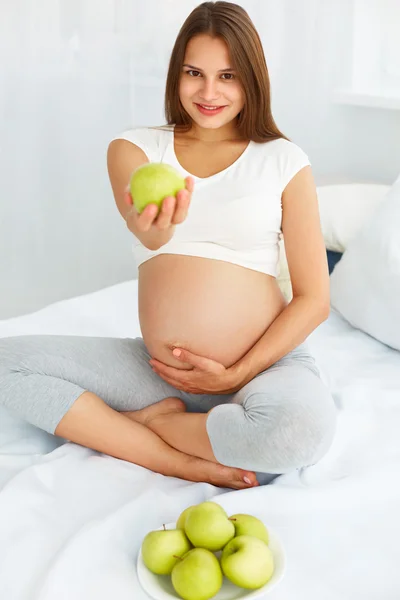 Jeune femme enceinte tenant Apple assis sur le lit. Hea ! — Photo